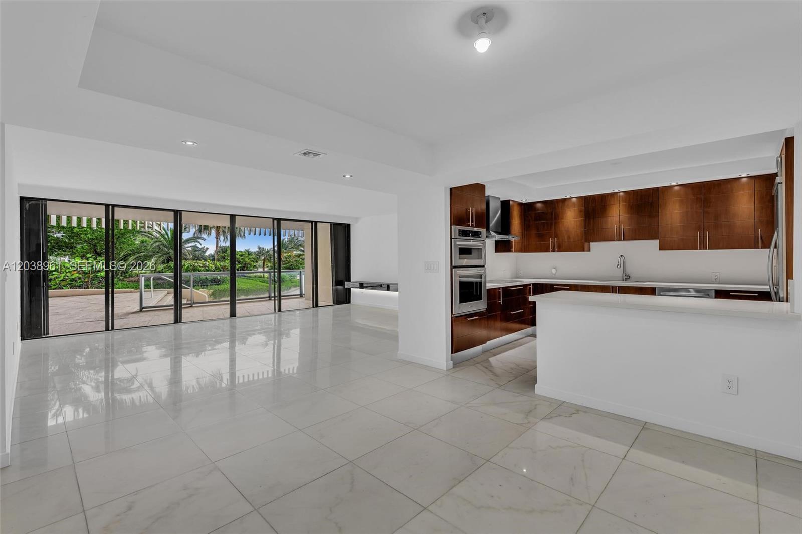 A modern kitchen with wood cabinets and a white island opens to a spacious living area — 2 Grove Isle Dr # B205, Miami FL 33133, MIAMI, FL