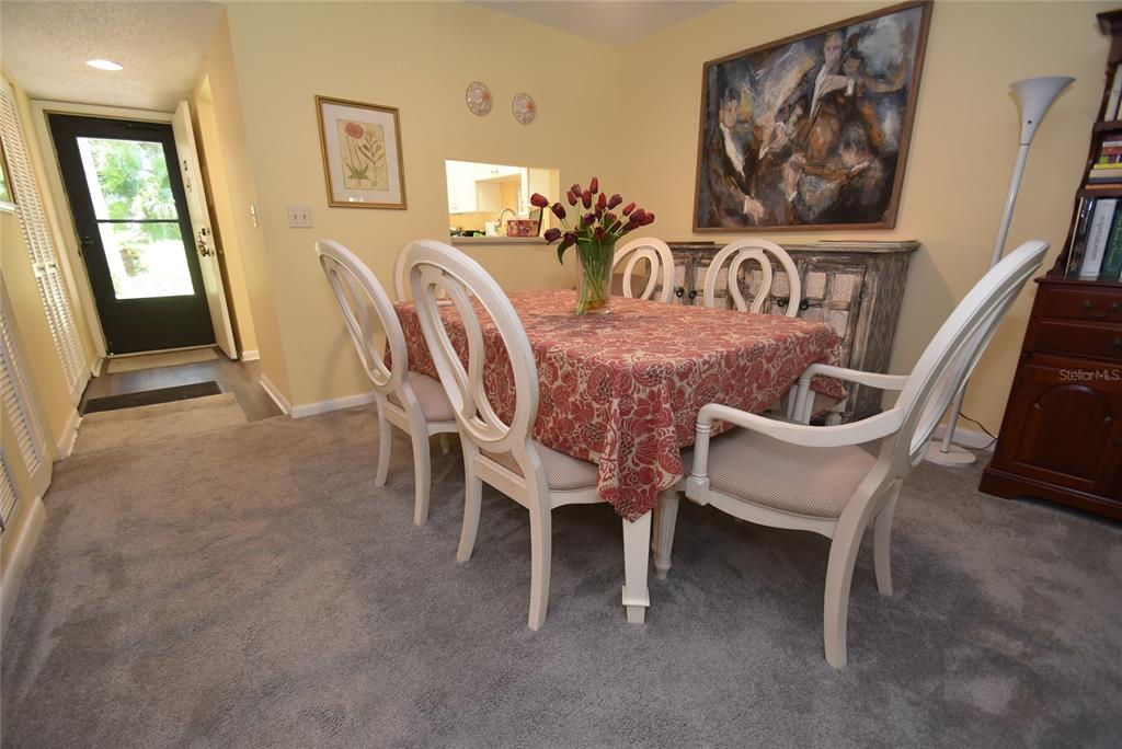 A dining room features a table with a floral tablecloth, six chairs, and gray carpeting — 1516 PELICAN COVE ROAD UNIT GR144, SARASOTA, FL