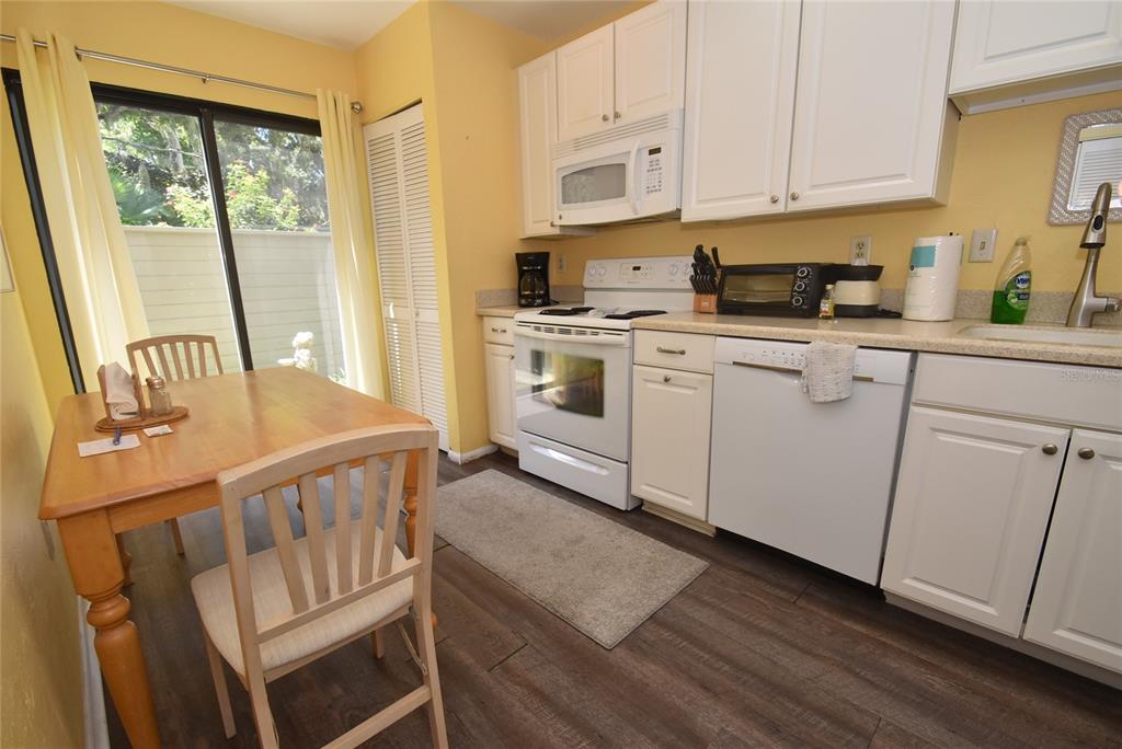 A kitchen with white cabinets, white appliances, a dining table, and sliding glass doors — 1516 PELICAN COVE ROAD UNIT GR144, SARASOTA, FL