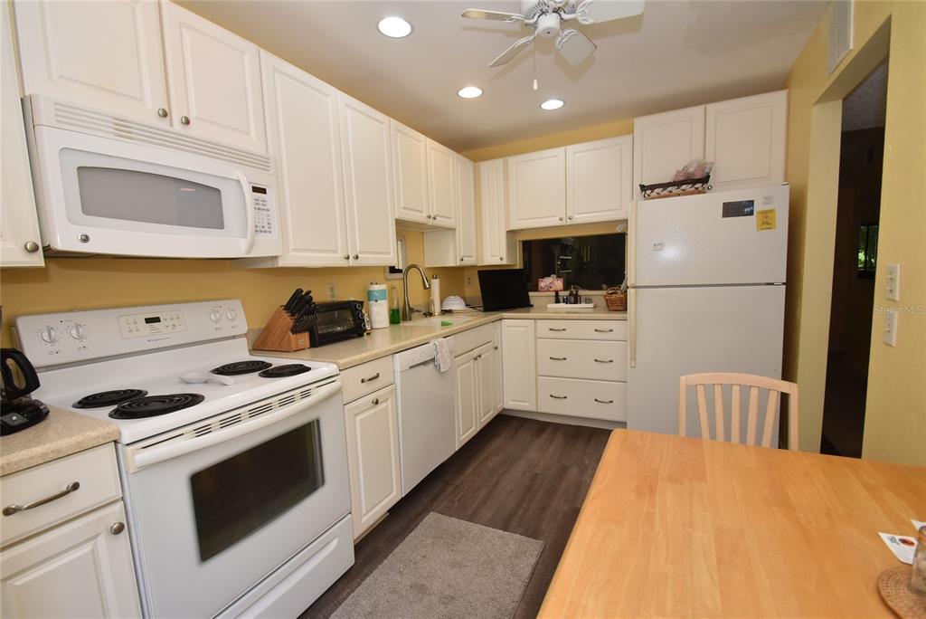 A kitchen with white cabinets, white appliances, light countertops, and wood-look flooring — 1516 PELICAN COVE ROAD UNIT GR144, SARASOTA, FL