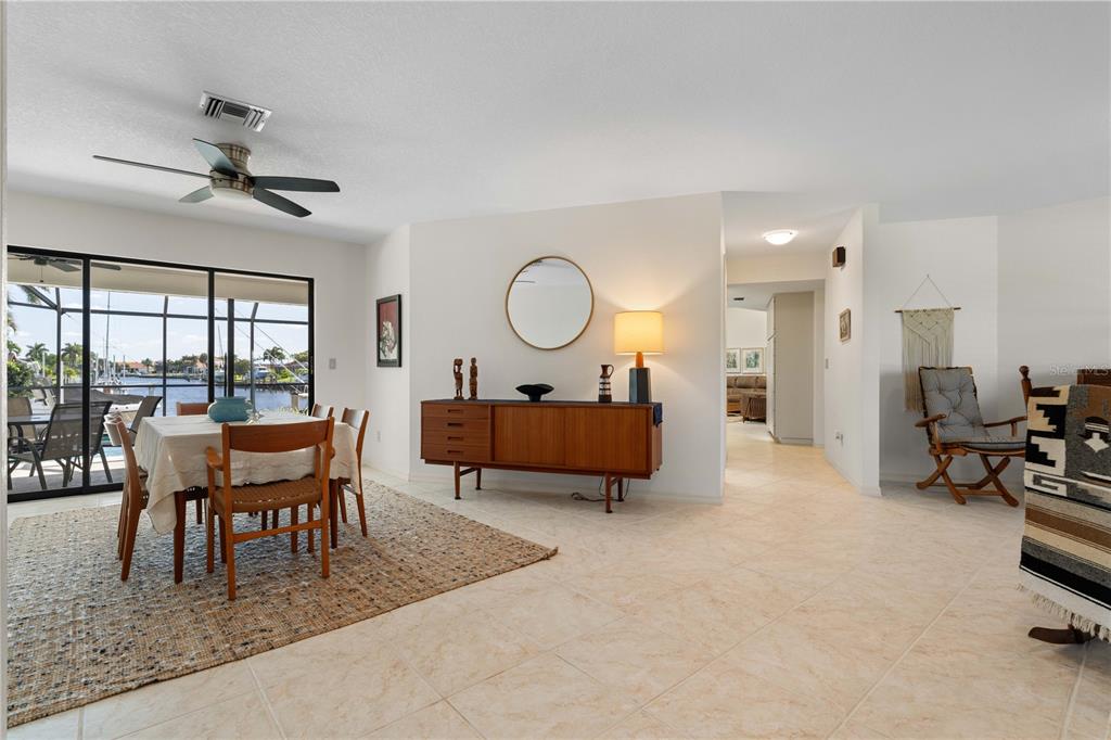 A dining area with a wooden sideboard, round mirror, and sliding doors overlooking a canal — 308 COLONY POINT DRIVE, PUNTA GORDA, FL