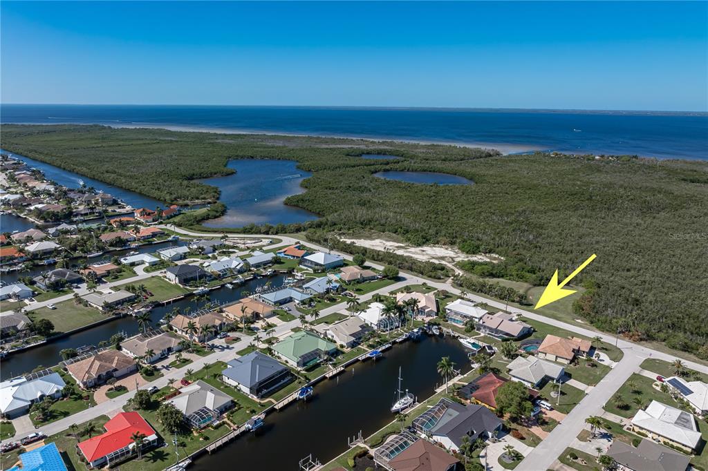 An aerial view shows a residential neighborhood with canal-front homes bordering a large wooded area — 308 COLONY POINT DRIVE, PUNTA GORDA, FL