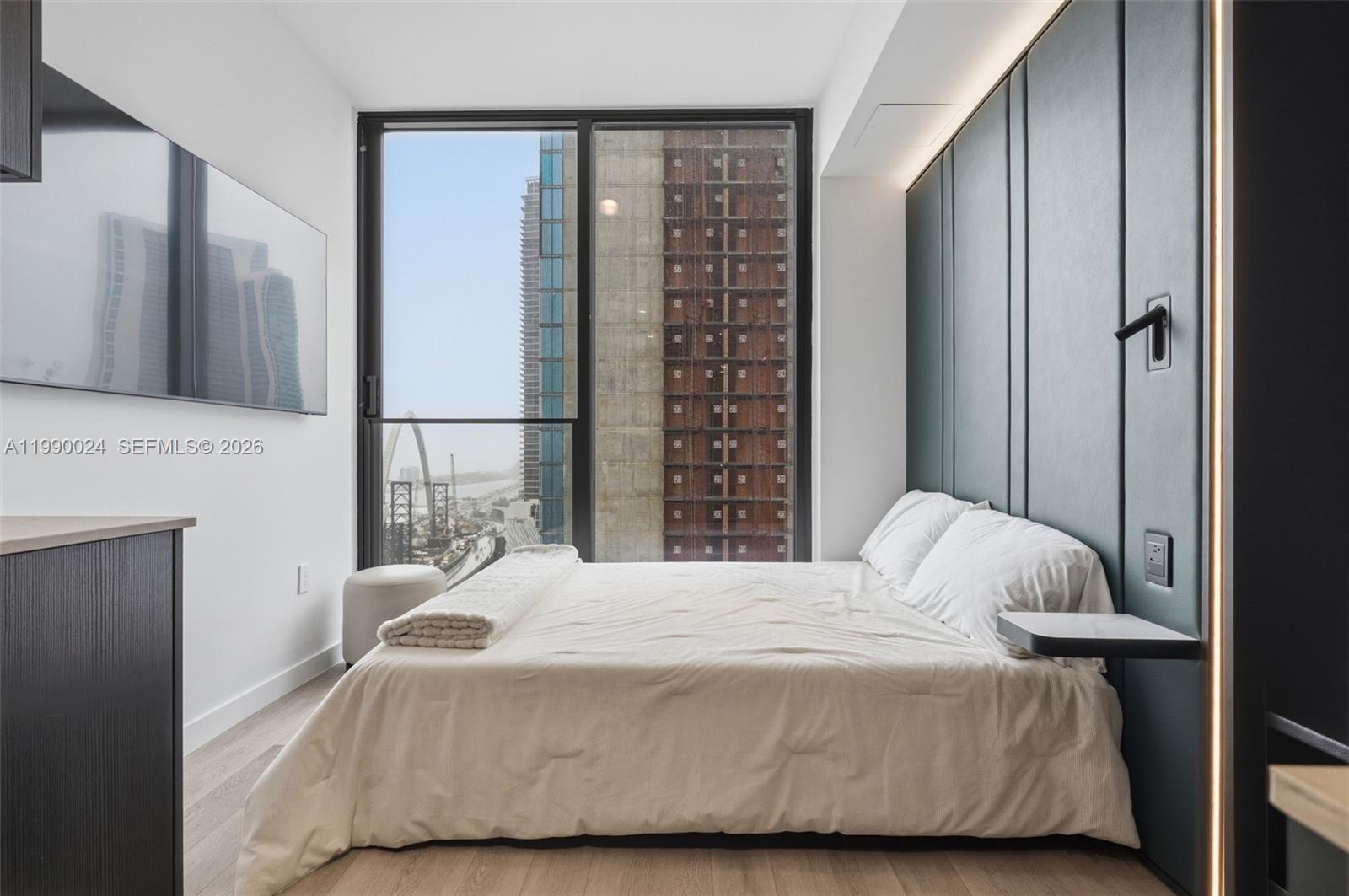 A modern bedroom features a bed against a dark paneled wall with city views outside — 20 NE 11th St # 2306A, Miami FL 33132, MIAMI, FL