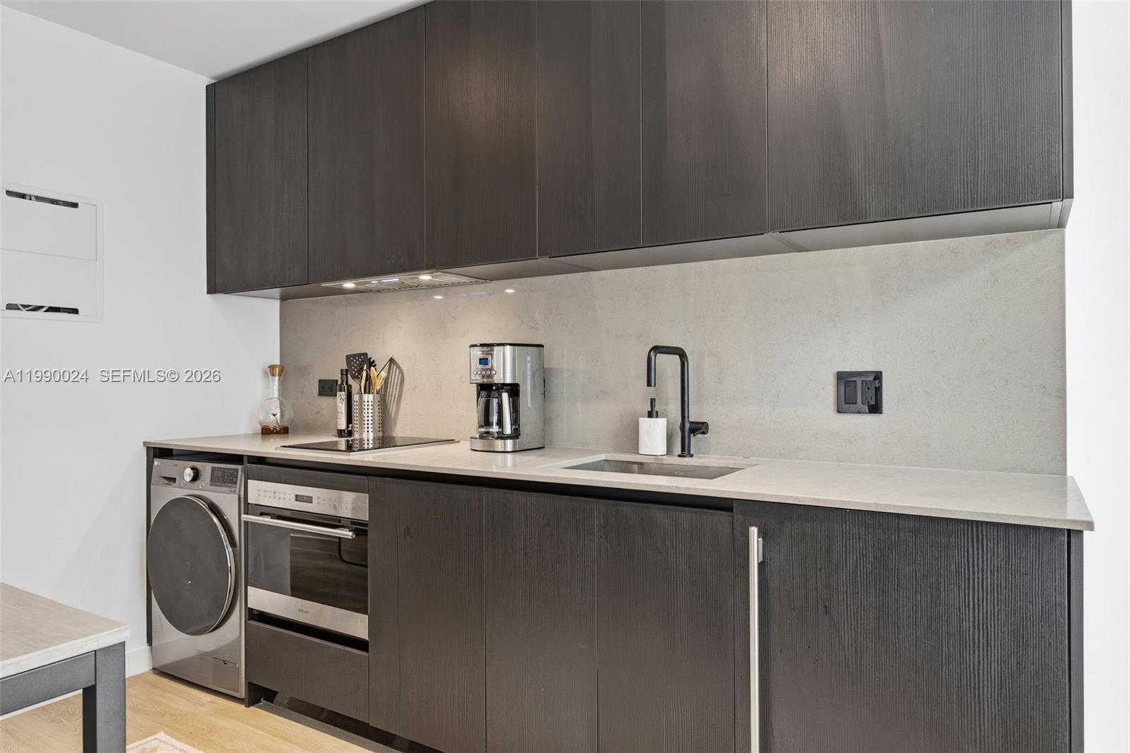 A modern kitchen features dark wood cabinetry, a light stone countertop, and an integrated washer — 20 NE 11th St # 2306A, Miami FL 33132, MIAMI, FL
