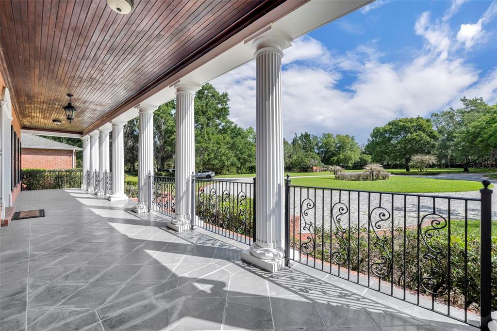 A covered porch features stone flooring, white columns, and black metal railings overlooking a lawn — 9726 KILGORE ROAD, ORLANDO, FL