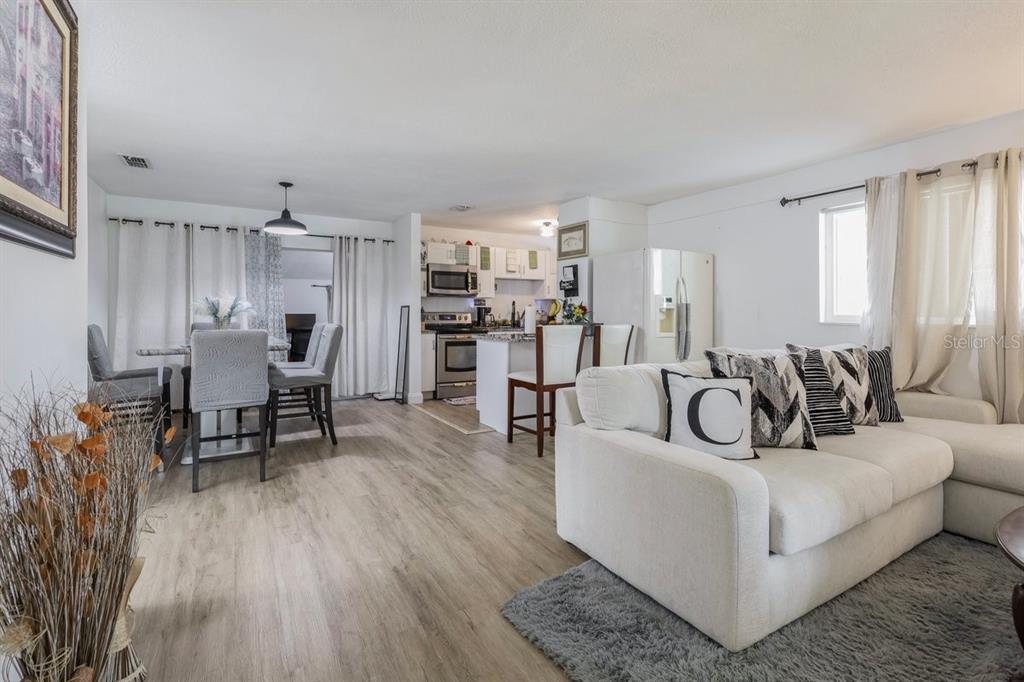 An open-concept living and dining area features light wood-look flooring and a white kitchen — 4725 CEPEDA STREET, ORLANDO, FL