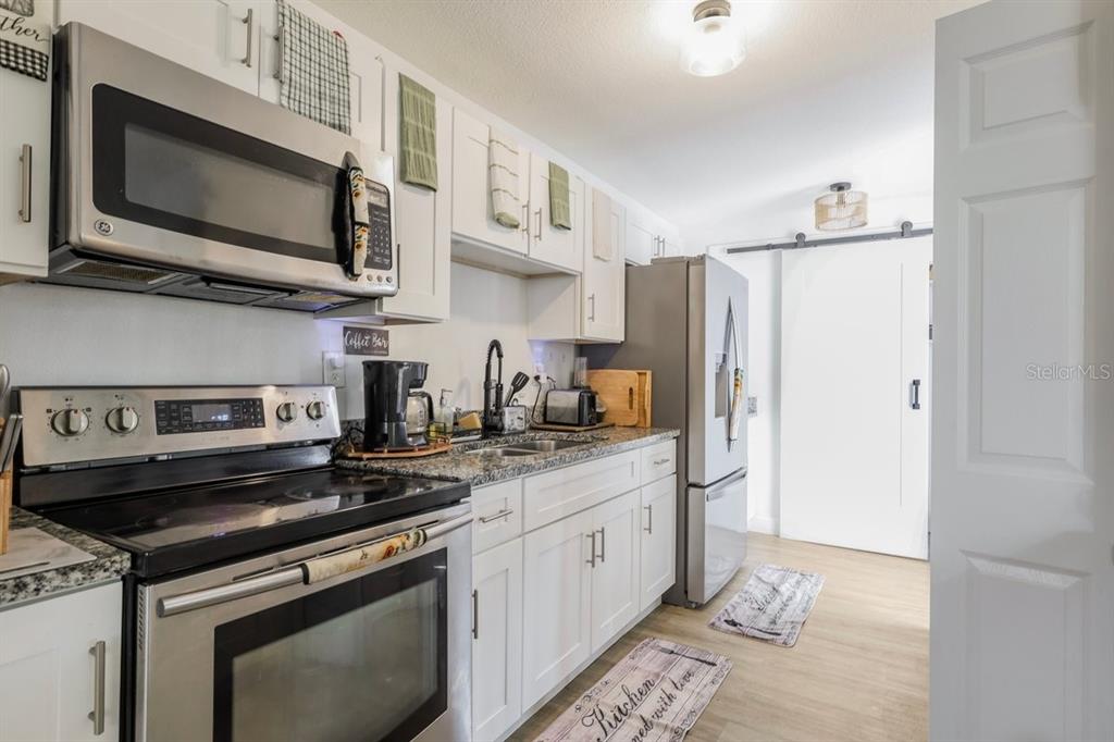 A kitchen features white cabinets, stainless steel appliances, granite countertops, and a sliding barn door — 4725 CEPEDA STREET, ORLANDO, FL