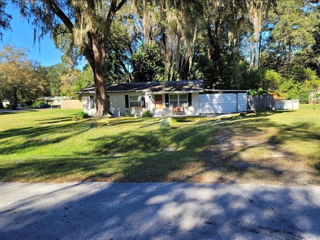 A single-story house with a light-colored exterior, a metal carport, and large mossy oak trees — 4808 NE 3RD PLACE, GAINESVILLE, FL