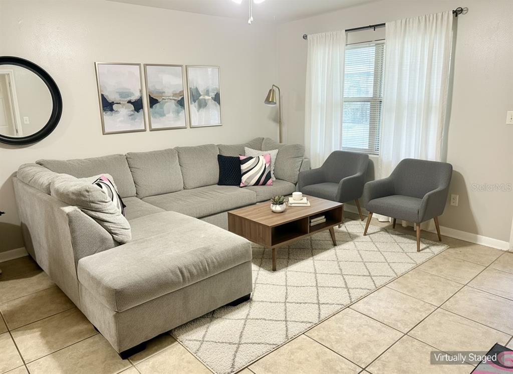 This virtually staged living room features a gray sectional, two armchairs, and a coffee table — 4808 NE 3RD PLACE, GAINESVILLE, FL