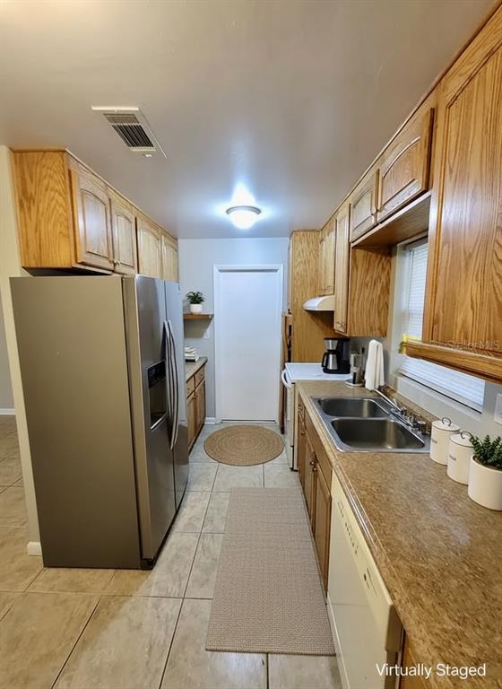 A galley kitchen features oak cabinets, stainless steel appliances, and tile flooring — 4808 NE 3RD PLACE, GAINESVILLE, FL