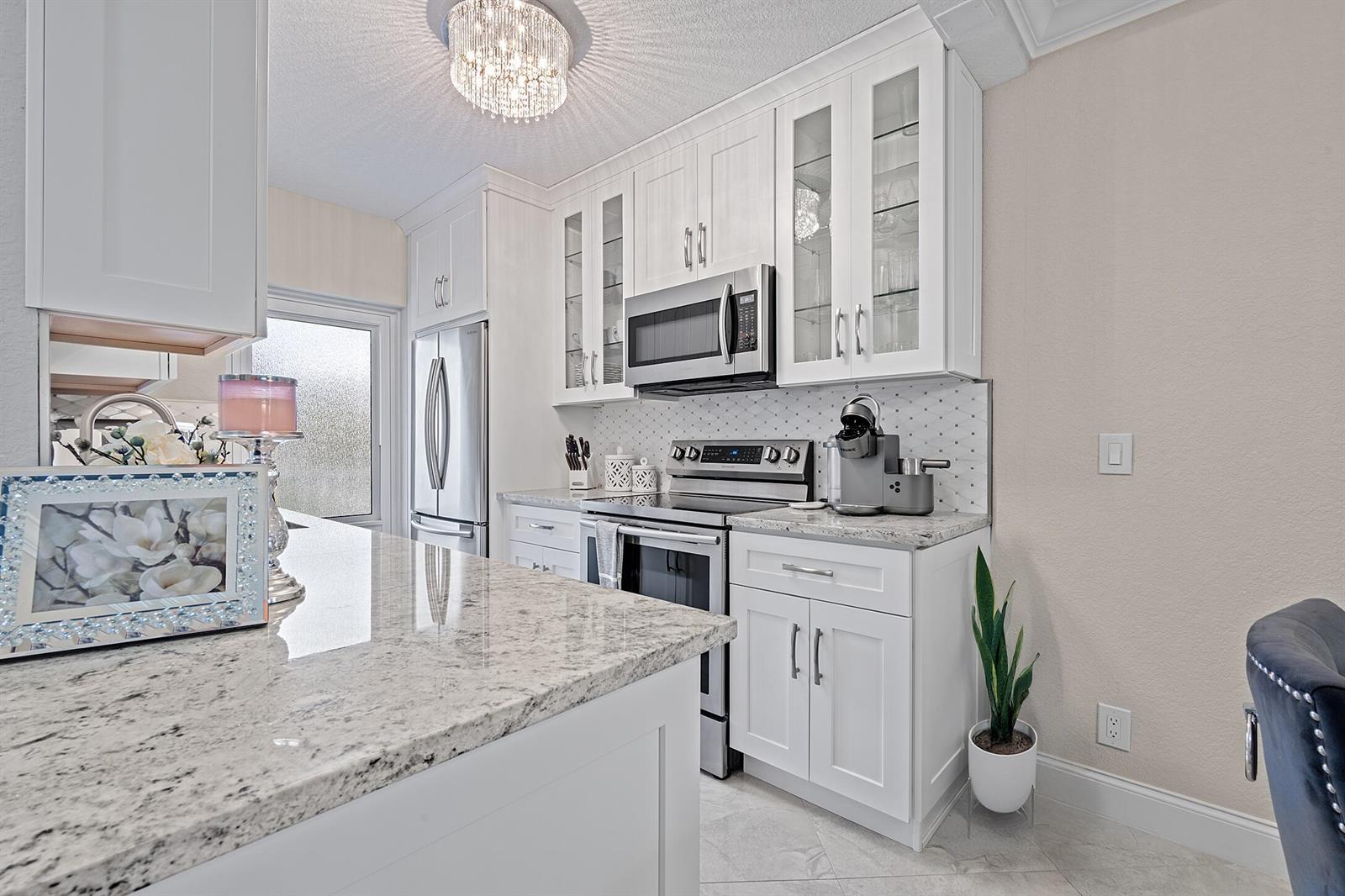 A bright kitchen features white cabinets, granite countertops, stainless steel appliances, and a crystal chandelier — 1910 S Ocean Boulevard # 204, Delray Beach FL 33483, DELRAY BEACH, FL