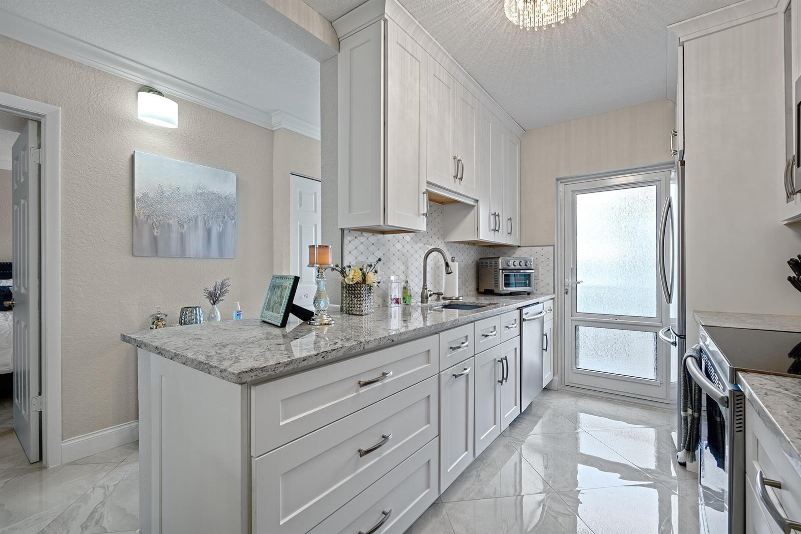 A bright kitchen features white cabinetry, granite countertops, and light-colored tile flooring — 1910 S Ocean Boulevard # 204, Delray Beach FL 33483, DELRAY BEACH, FL
