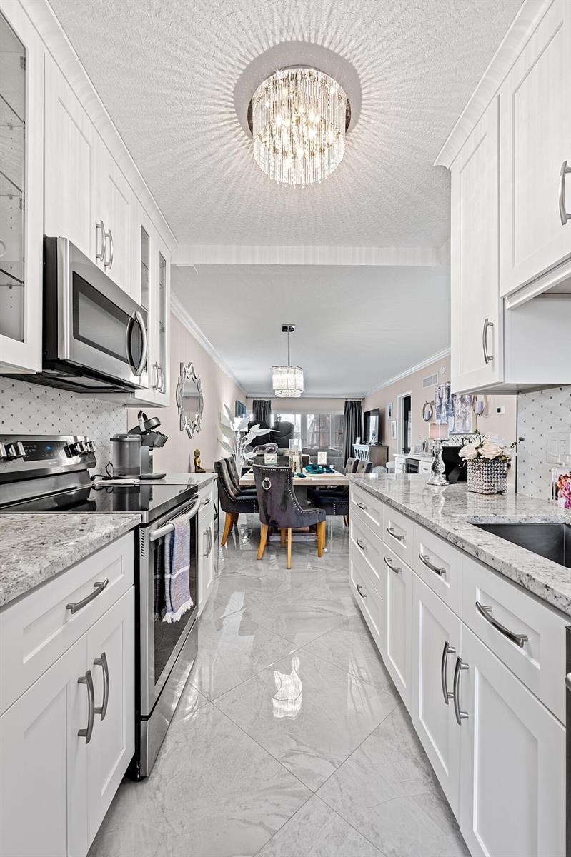 A modern white kitchen with granite countertops leads into a dining area with a chandelier — 1910 S Ocean Boulevard # 204, Delray Beach FL 33483, DELRAY BEACH, FL