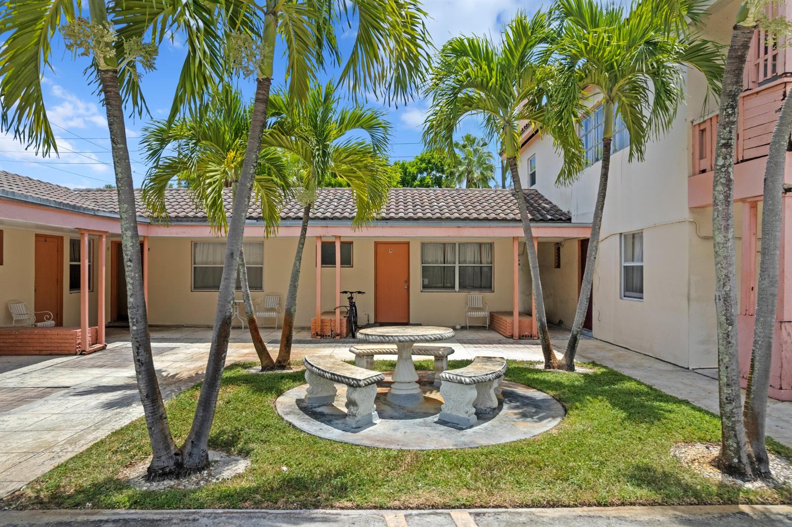 A courtyard with a stone table and benches sits between palm trees and apartment units — 7800 S Dixie Highway, West Palm Beach FL 33405, WEST PALM BEACH, FL