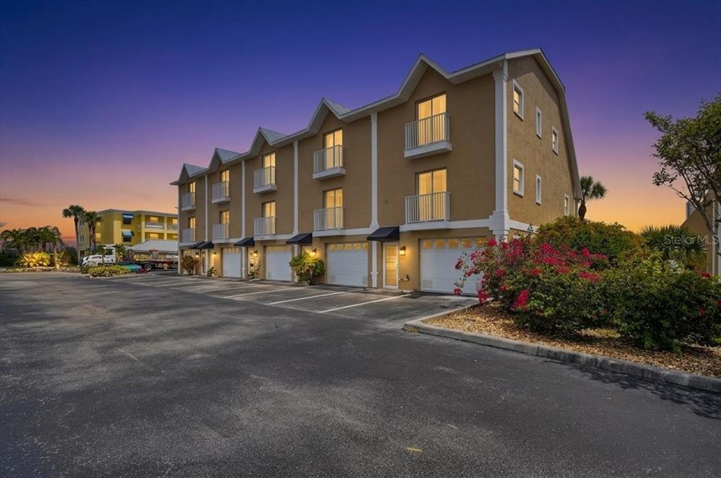 A multi-story tan townhouse building with attached garages and balconies at dusk — 1950 OREGON TRAIL UNIT 1A, ENGLEWOOD, FL