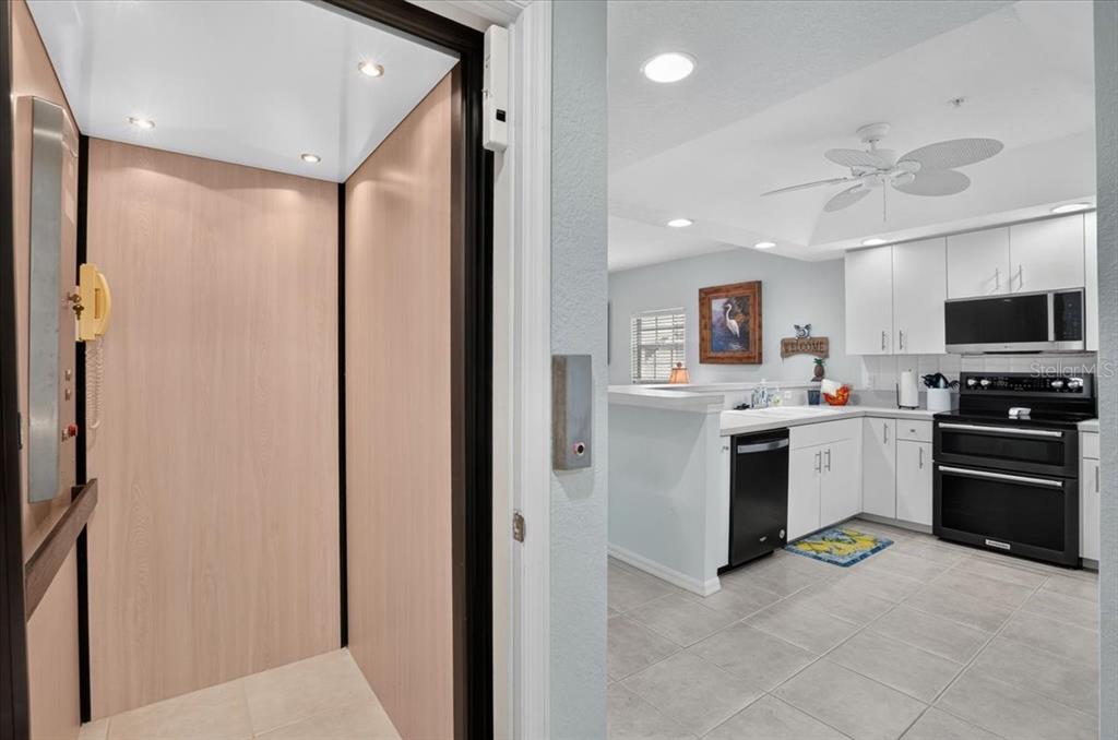 An elevator opens into a kitchen with white cabinets, black appliances, and tile flooring — 1950 OREGON TRAIL UNIT 1A, ENGLEWOOD, FL
