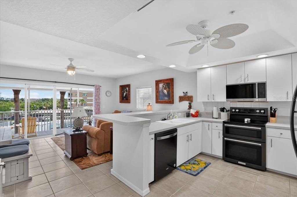 A kitchen with white cabinets and black appliances overlooks a living area with a balcony — 1950 OREGON TRAIL UNIT 1A, ENGLEWOOD, FL