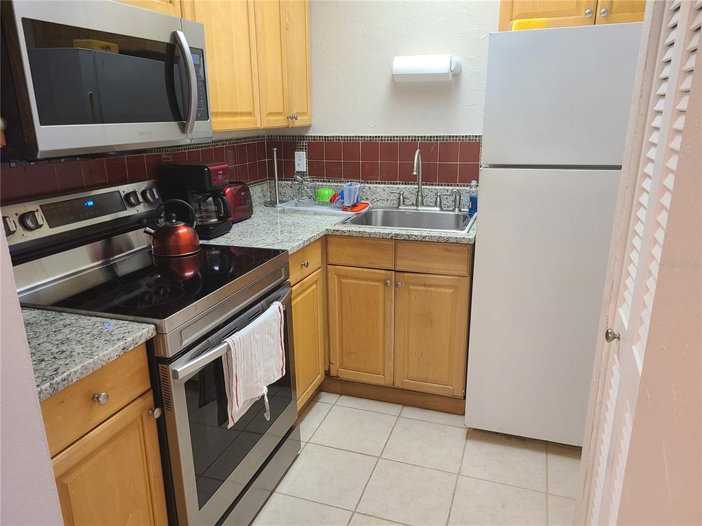 A kitchen features wood cabinets, granite countertops, stainless steel appliances, and a tiled backsplash — 2763 WOODGATE LANE UNIT 207, SARASOTA, FL
