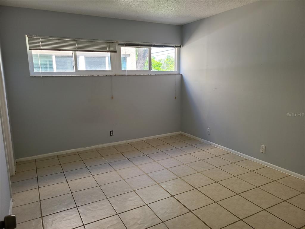 An empty room features light gray walls, beige tile flooring, and a horizontal window — 2763 WOODGATE LANE UNIT 207, SARASOTA, FL