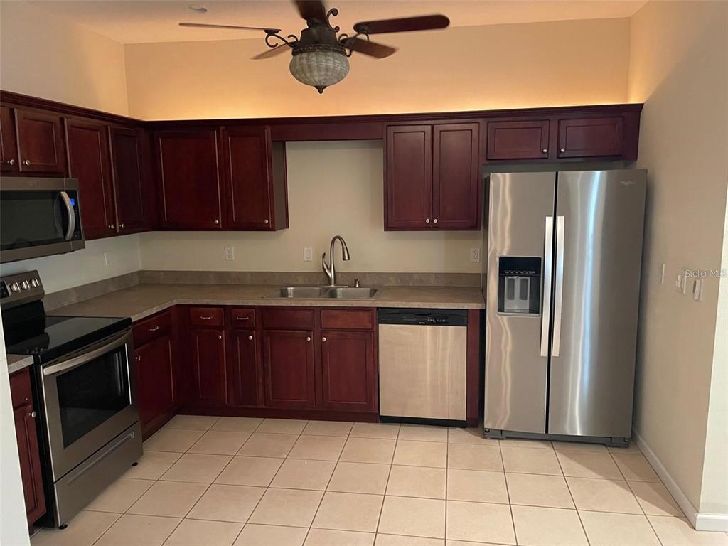 A kitchen features dark wood cabinets, stainless steel appliances, and light-colored tile flooring — 9035 VISTA VERDE DRIVE, PALMETTO, FL