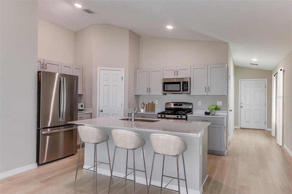 A kitchen features light gray cabinets, stainless steel appliances, a center island, and wood flooring — 4430 RIVERBEND BOULEVARD, HAINES CITY, FL