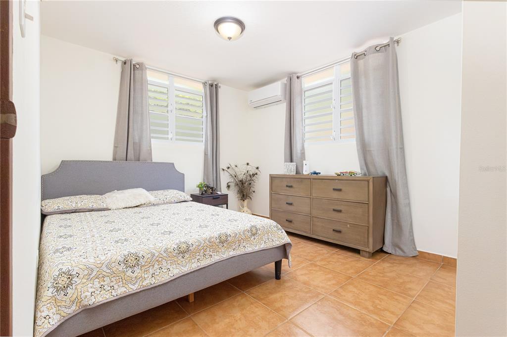 A bedroom features a gray upholstered bed, a wooden dresser, and tile flooring — 339 ST BO MONTOSO UNIT 145, MAYAGUEZ, PR