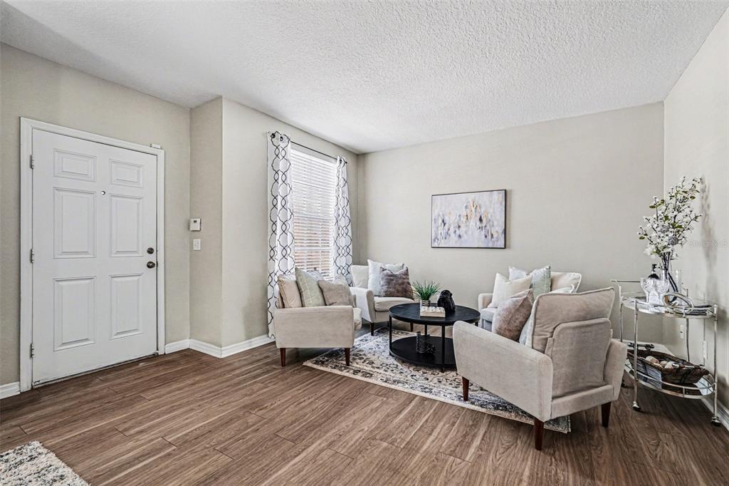 A living room features light walls, wood-look flooring, four armchairs, and a central coffee table — 3342 BROKEN BOW DRIVE, LAND O LAKES, FL