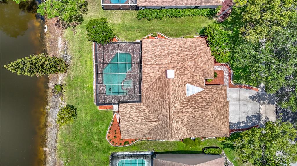An aerial view shows a house with a screened pool, brown roof, and lakefront yard — 16040 PENWOOD DRIVE, TAMPA, FL