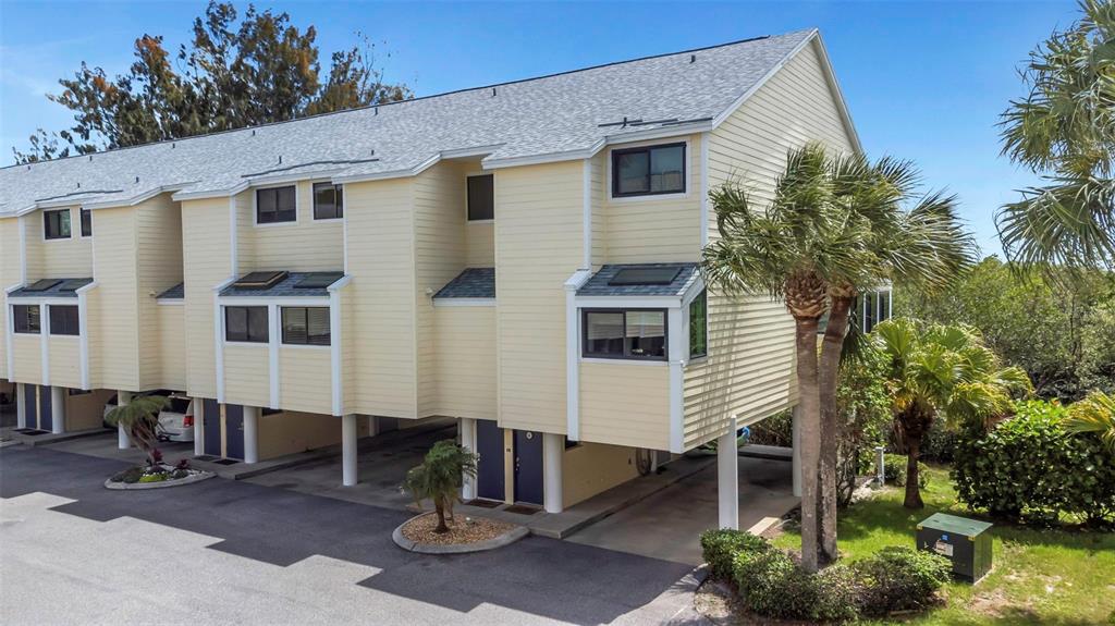 An exterior view of a yellow multi-story townhouse elevated on stilts with covered parking underneath — 1500 SUNSET ROAD UNIT F7, TARPON SPRINGS, FL