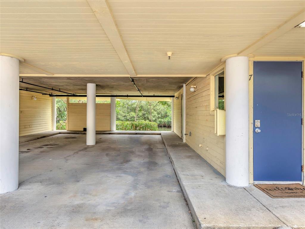 A covered carport area features concrete flooring, white support columns, and a blue entry door — 1500 SUNSET ROAD UNIT F7, TARPON SPRINGS, FL