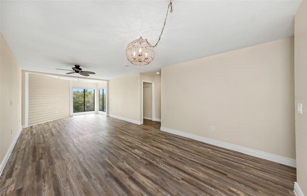 An empty room with wood-look flooring, a ceiling fan, and a decorative globe pendant light — 1500 SUNSET ROAD UNIT F7, TARPON SPRINGS, FL