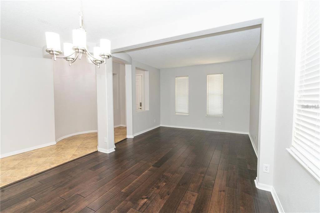 A dining area with tile flooring transitions into a living room with dark wood floors — 9763 MOSS ROSE WAY, ORLANDO, FL