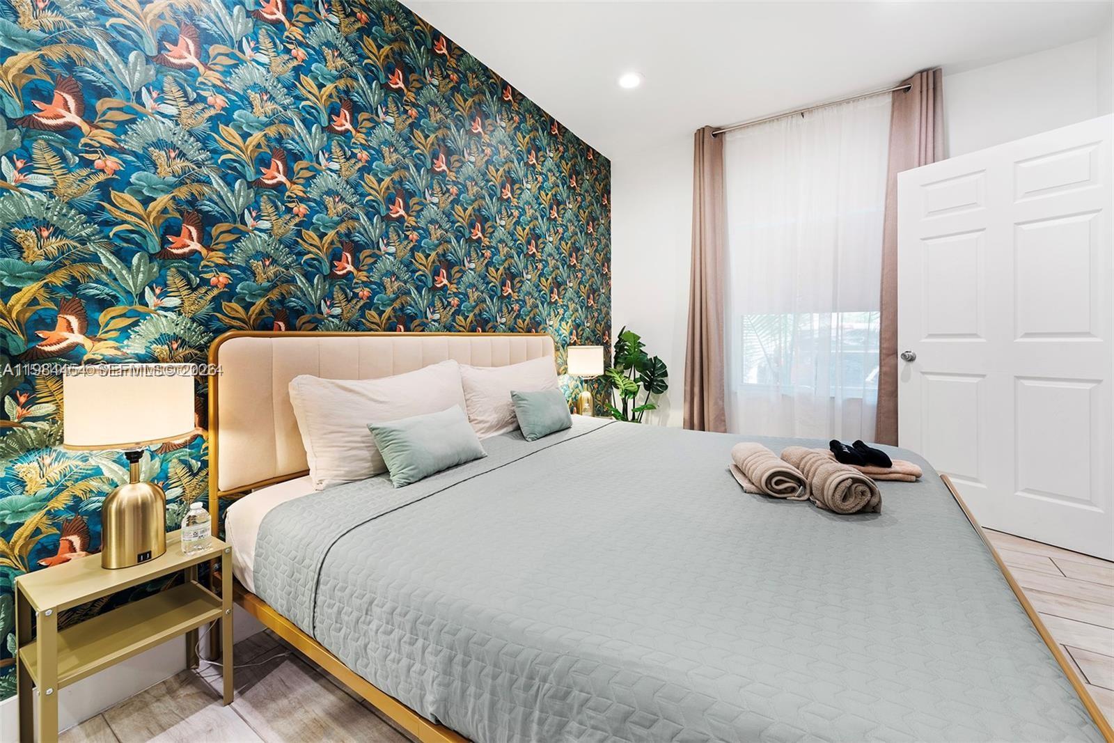 A bedroom features a bed against a wall with vibrant, tropical-patterned wallpaper — 232 NW 59th St, Miami FL 33127, MIAMI, FL