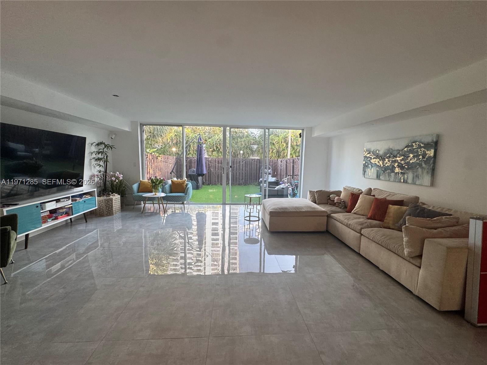 A spacious living room features large floor tiles, a sectional sofa, and sliding glass doors — 2308 NE 7th St # 29, Hallandale Beach FL 33009, HALLANDALE BEACH, FL