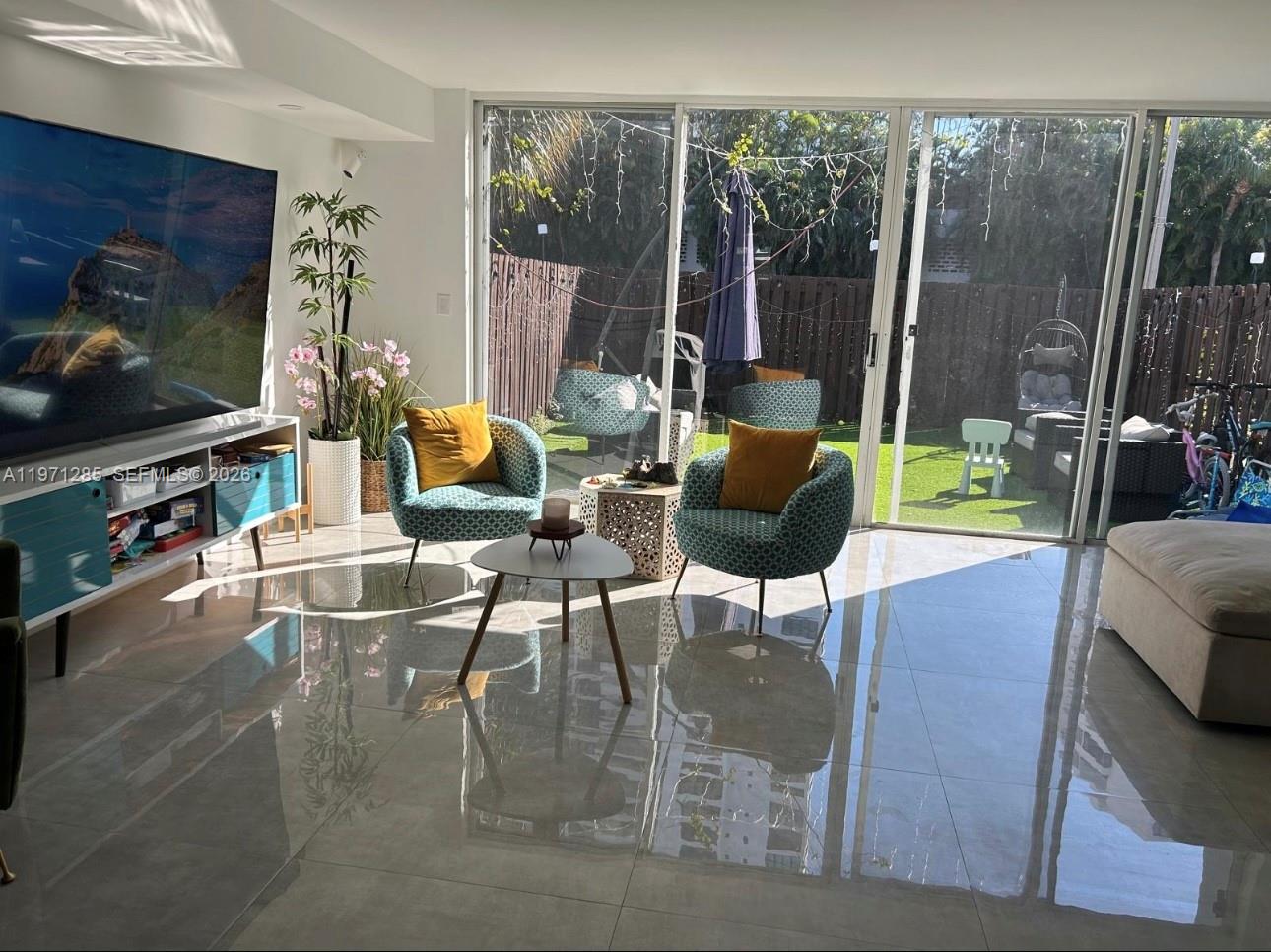 A living room features tiled floors, two patterned armchairs, and sliding glass doors to a yard — 2308 NE 7th St # 29, Hallandale Beach FL 33009, HALLANDALE BEACH, FL
