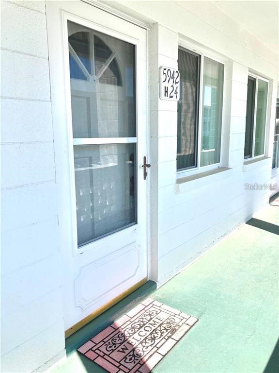 A white exterior door with a screen and a welcome mat on a porch — 5942 WELCOME ROAD UNIT H24, BRADENTON, FL