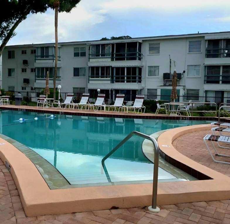 A swimming pool with lounge chairs sits in front of a multi-story apartment building — 5942 WELCOME ROAD UNIT H24, BRADENTON, FL