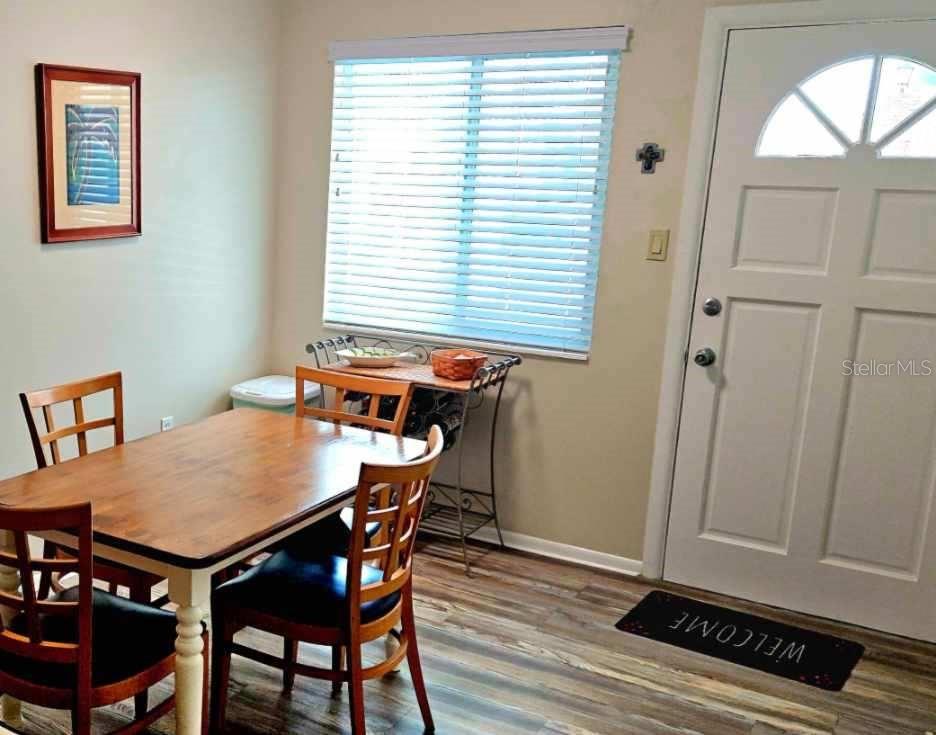 A dining area features a wooden table, chairs, a window with blinds, and a front door — 5942 WELCOME ROAD UNIT H24, BRADENTON, FL