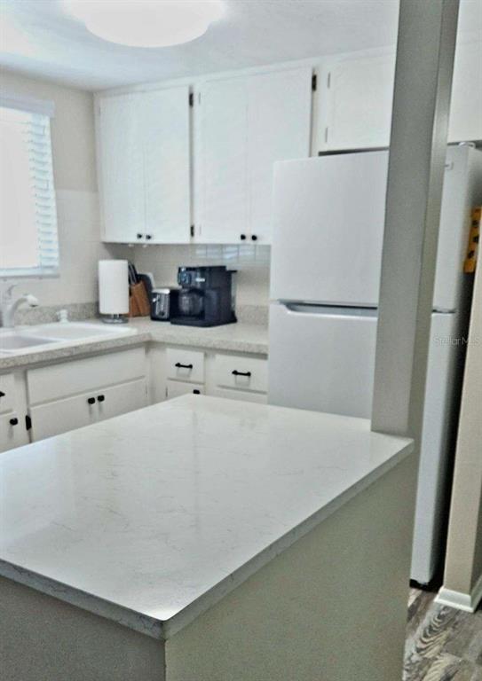 A kitchen features white cabinets, a white refrigerator, and a light-colored countertop peninsula — 5942 WELCOME ROAD UNIT H24, BRADENTON, FL