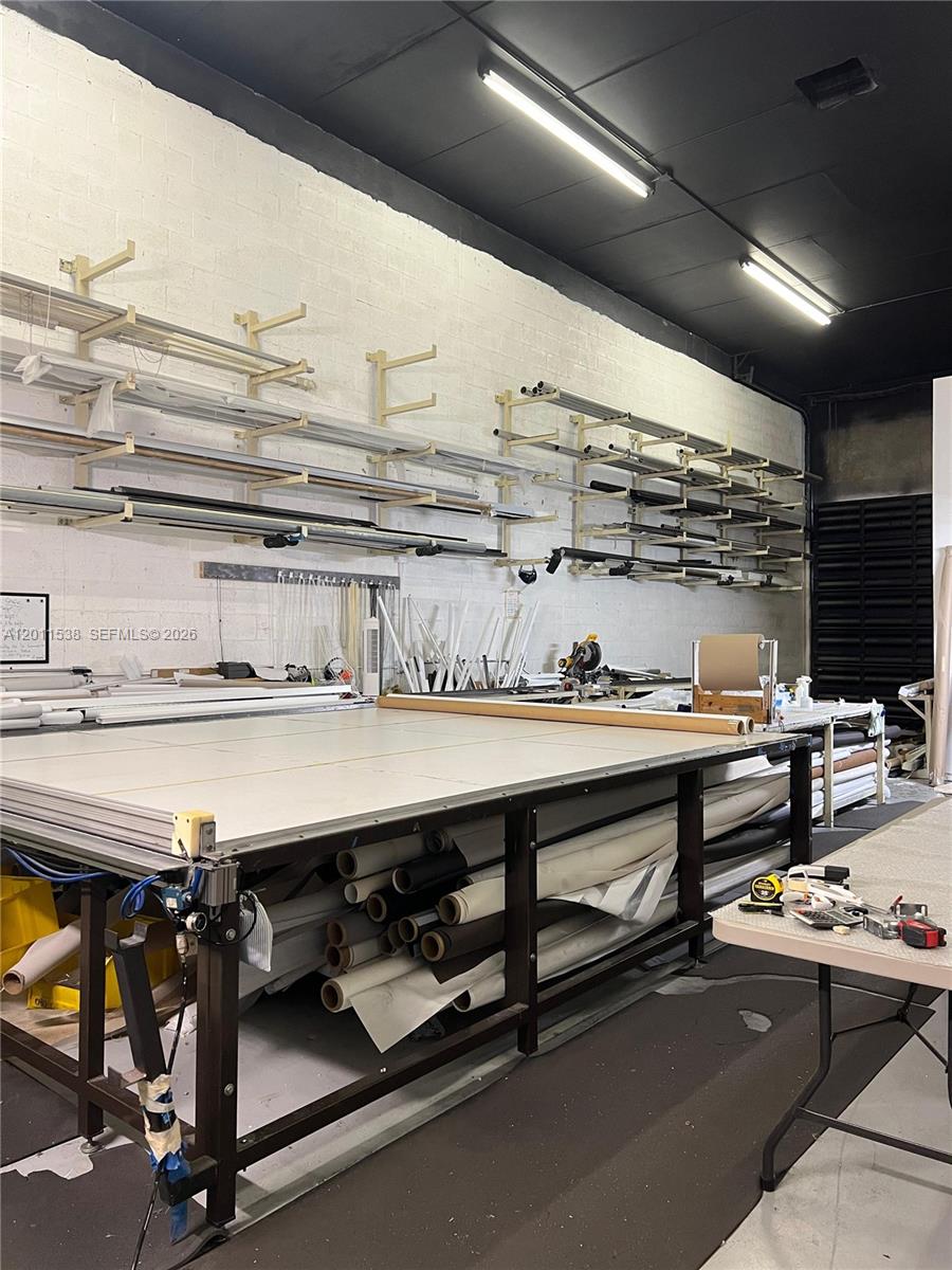 A workshop features a large central cutting table, wall-mounted storage racks, and rolls of material — 13210 SW 132nd Ave, Miami FL 33186, MIAMI, FL