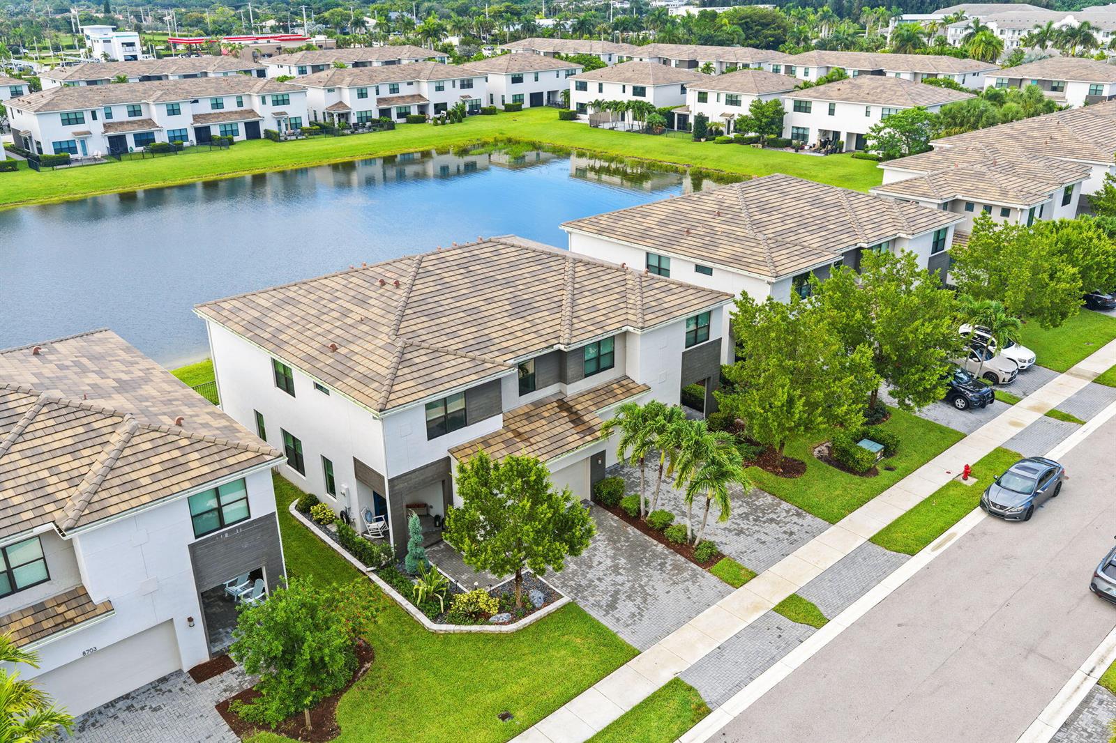 An aerial view shows modern townhouses with tiled roofs situated along a community lake — 8697 Corvus, Lake Worth FL 33467, LAKE WORTH, FL