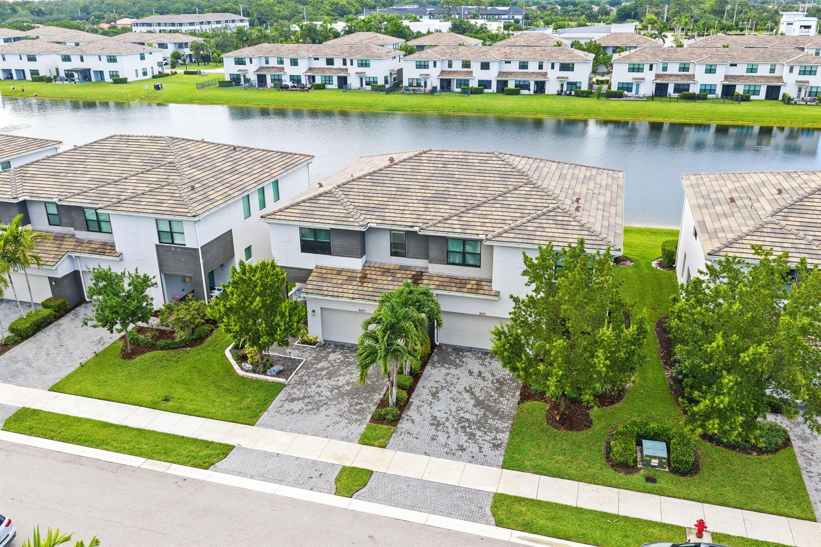 An aerial view shows two-story townhomes with tiled roofs, paved driveways, and a waterfront backyard — 8697 Corvus, Lake Worth FL 33467, LAKE WORTH, FL