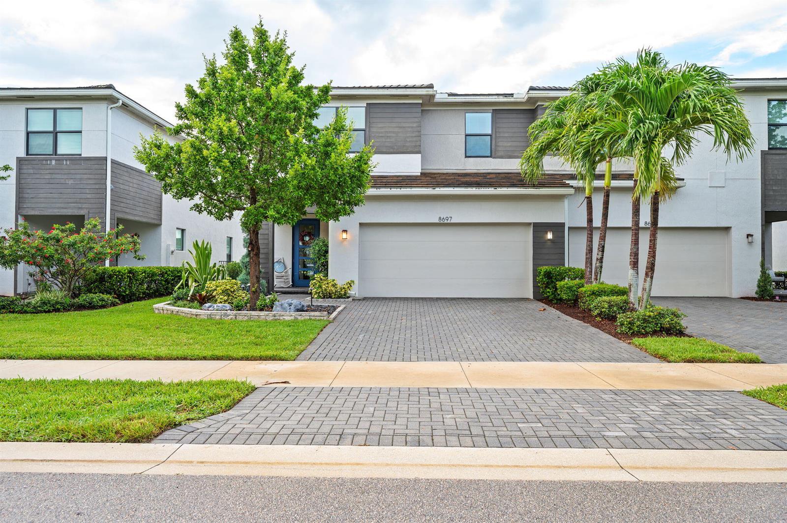 A two-story townhouse features a paved driveway, a two-car garage, and a front garden — 8697 Corvus, Lake Worth FL 33467, LAKE WORTH, FL