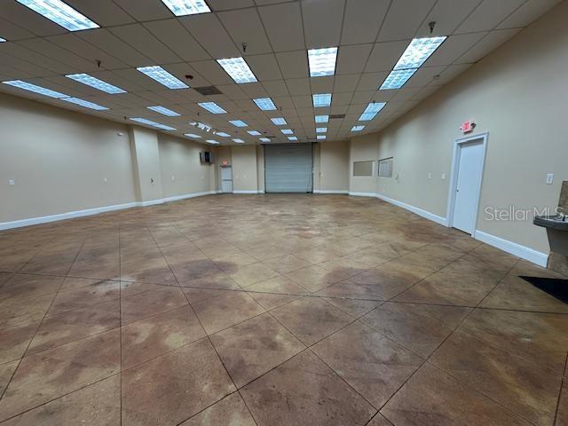 An empty commercial space features a stained concrete floor, drop ceiling, and a roll-up door — 350 ANCHOR ROAD UNIT 1050, CASSELBERRY, FL