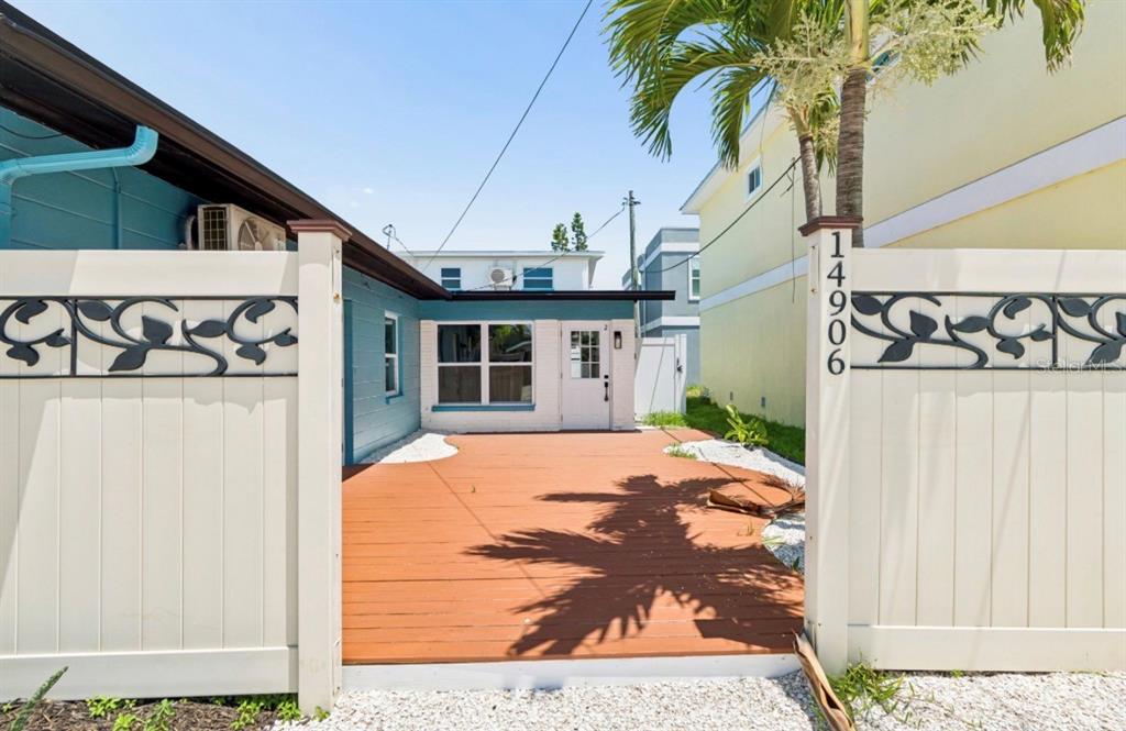A wooden deck sits between two white fences in front of a blue and white house — 14906 N BAYSHORE DRIVE, MADEIRA BEACH, FL