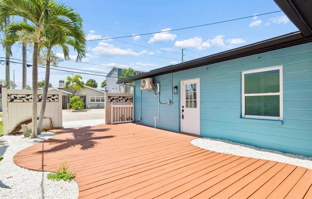 A turquoise house exterior features a wooden deck, white fencing, and palm trees — 14906 N BAYSHORE DRIVE, MADEIRA BEACH, FL