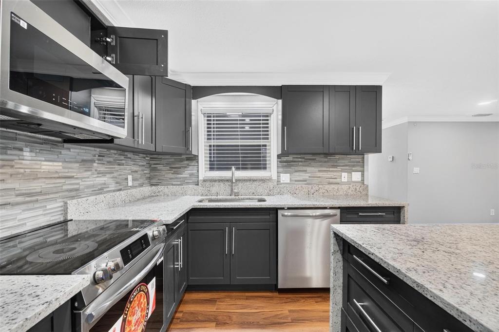 A kitchen features dark gray cabinets, granite countertops, stainless steel appliances, and a tiled backsplash — 8700 58TH LANE N, PINELLAS PARK, FL