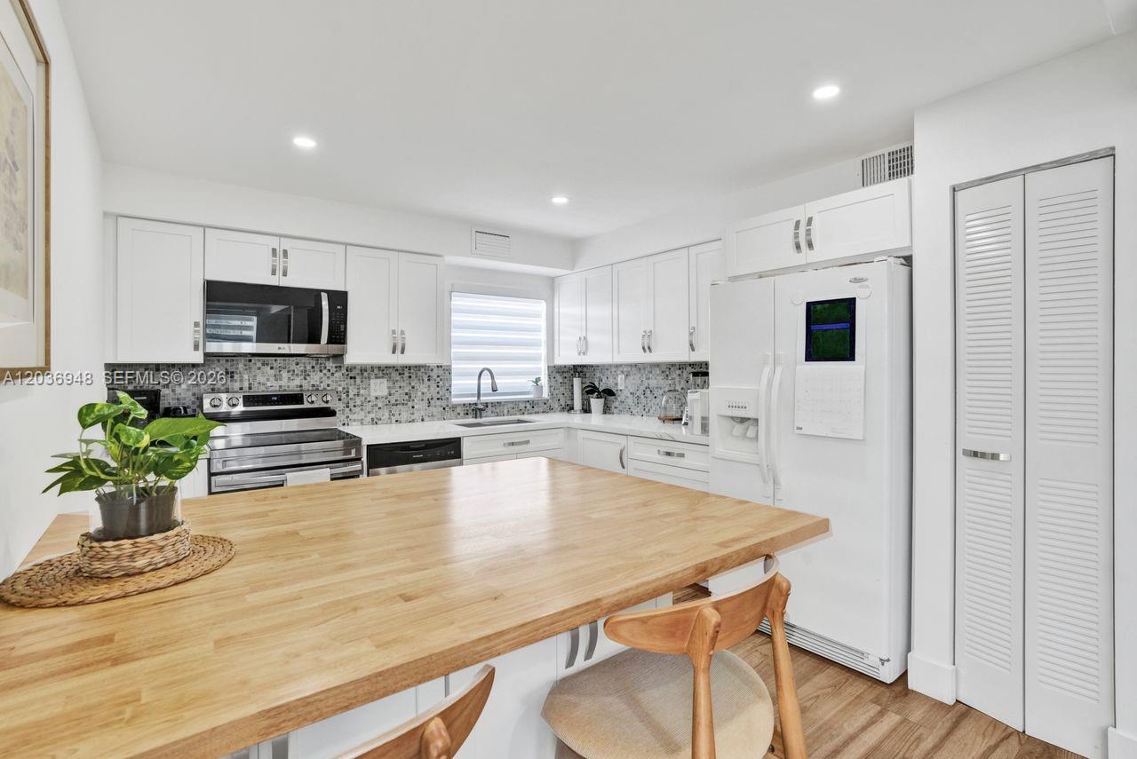 A kitchen features white cabinets, stainless steel appliances, a tiled backsplash, and a wooden island — 4555 SW 68th Ct Cir # 111, Miami FL 33155, MIAMI, FL
