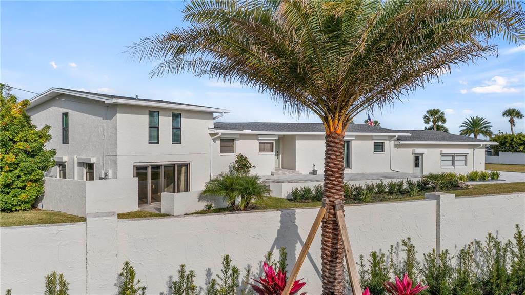 A white, two-story house with a palm tree in the foreground and a perimeter wall — 102 E CIRCLE DRIVE, NEW SMYRNA BEACH, FL