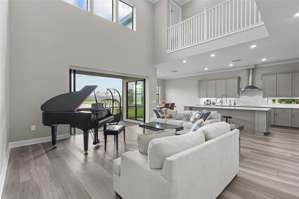 A grand piano sits in a high-ceilinged living room adjacent to an open-concept kitchen — 5855 SILVERSIDE PINE COURT, LAKEWOOD RANCH, FL